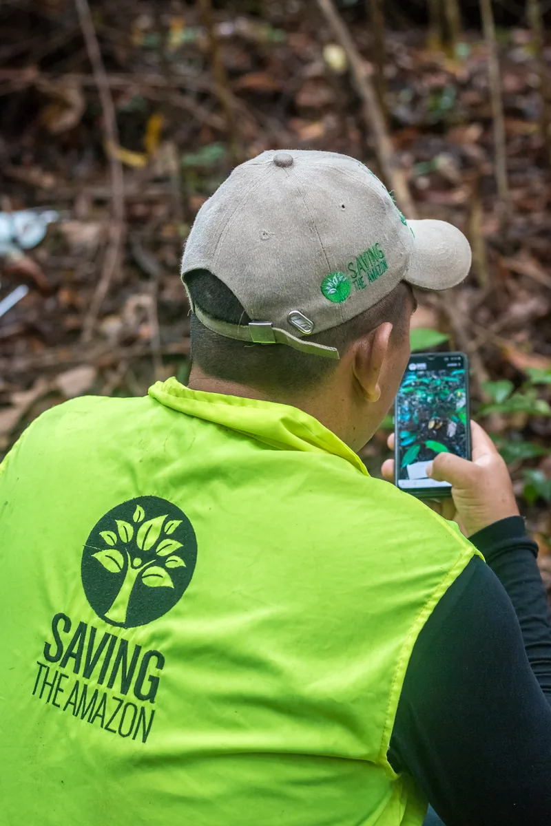 Integrante da equipe de campo da Saving The Amazon, com colete institucional, verificando uma foto no celular